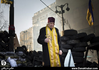یک کشیش اوکراینی در حال عبور از موانع خیابانی ایجاد شده از سوی معترضان حکومت (شهر کی یف)